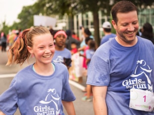Girls on the Run participant and coach smile while running at 5K celebration